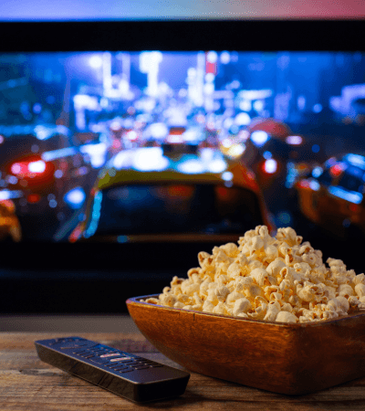 A bowl of popcorn in front of a TV playing a movie